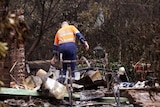 A policeman and forensics officer looks over a house where five people died at Kinglake