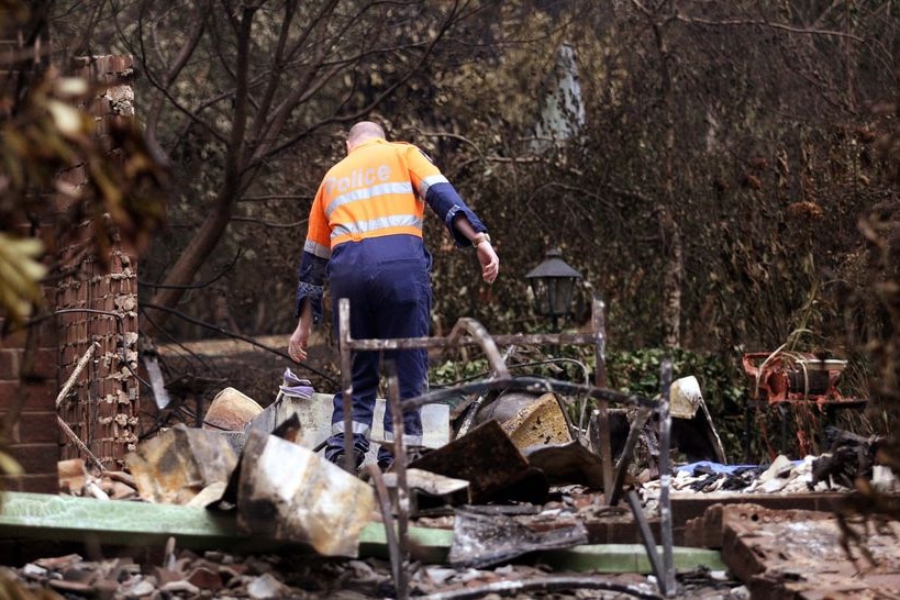 A policeman and forensics officer looks over a house where five people died at Kinglake