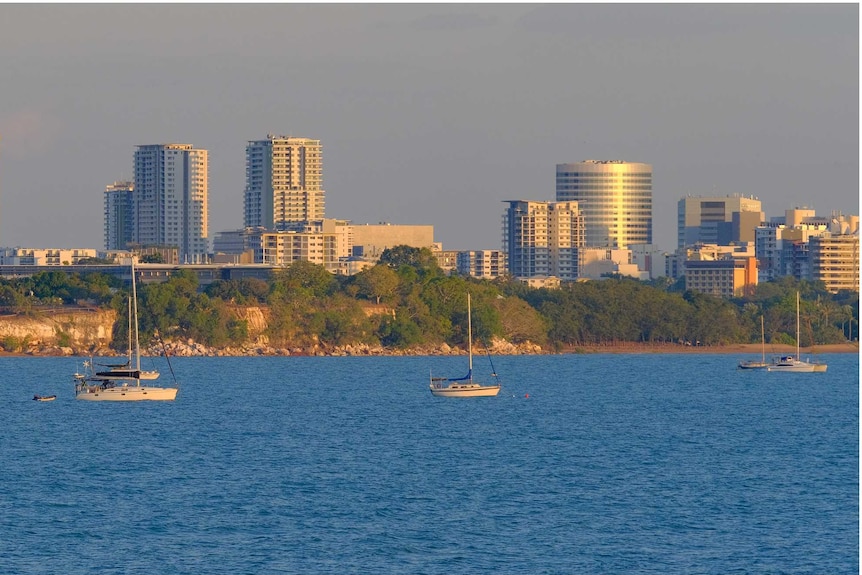 A view of the city from the sea with sunset light reflecting off the high-rise. Yachts are moored in the foreground.