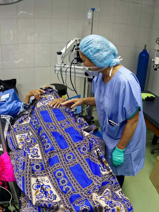 A person lies on an operating table covered in a blue patterned blanket.