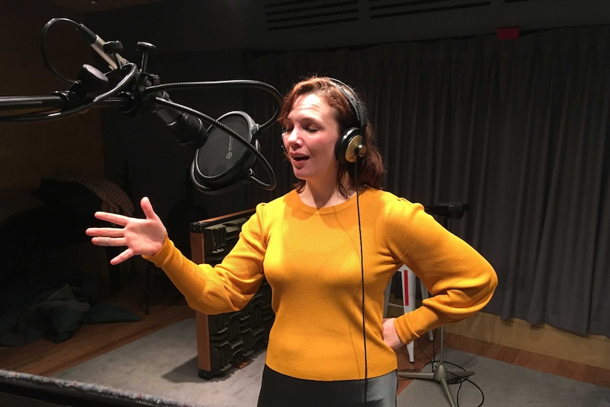 A white woman with red hair speaking into a microphone in a recording studio