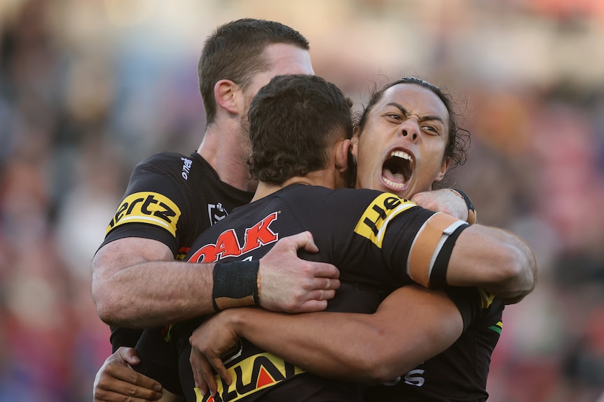 Jarome Luai shouts while being hugged by two Penrith Panthers teammates.