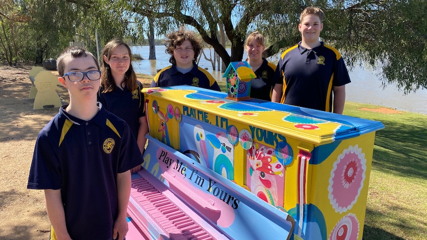 Four children stand around a brightly-painted piano. 