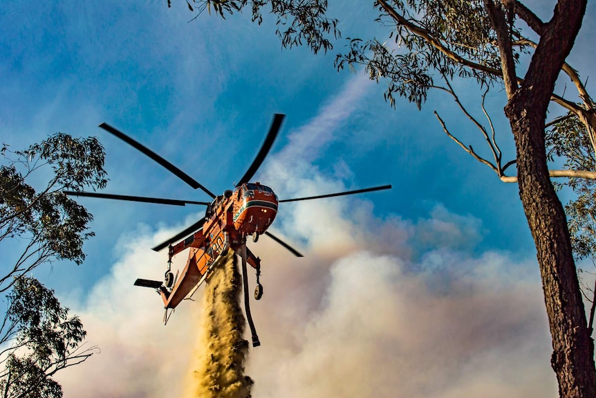 A helicopter drops liquid on a bushfire.