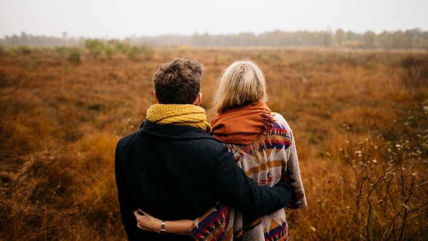 An unidentified couple stand in the middle of a big field.