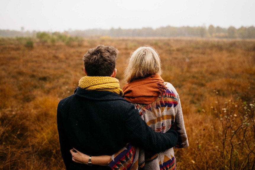 An unidentified couple stand in the middle of a big field.