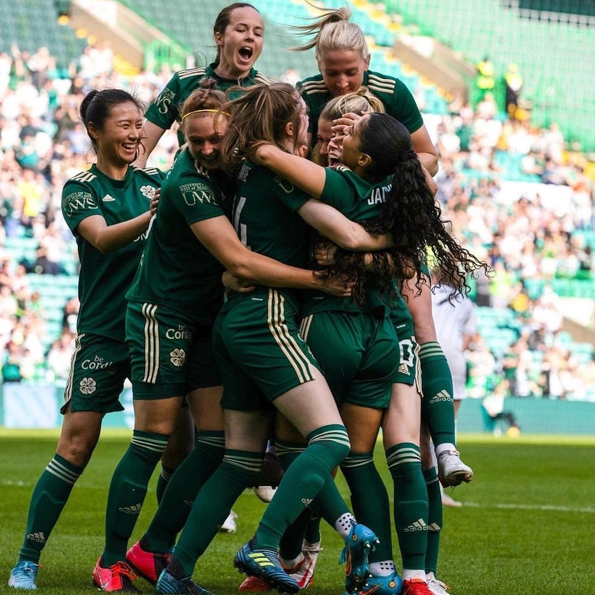 A group of women soccer players in green shirts hug each other