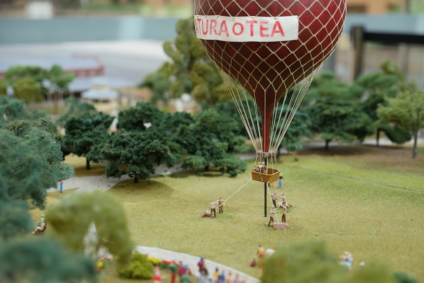 A miniature of a red hot air balloon taking off from a park surrounded by trees