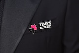 A pin reading Time's Up on a suit lapel.