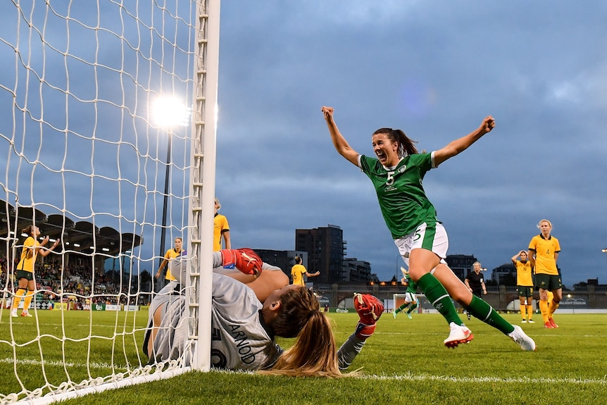 Niamh Fahey celebrates with her arms outstretched as a goalkeeper lies on the floor in front of her