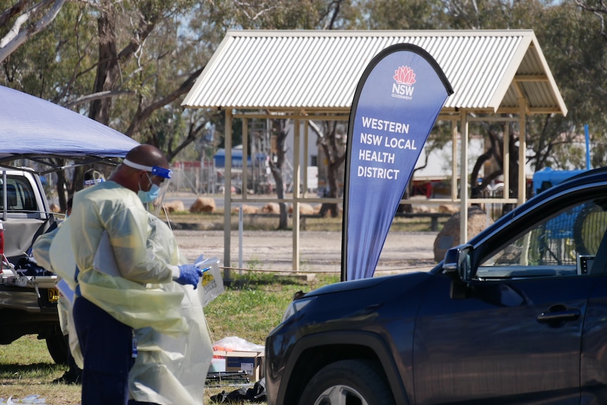 A medical worker in PPE attends to someone in a car.