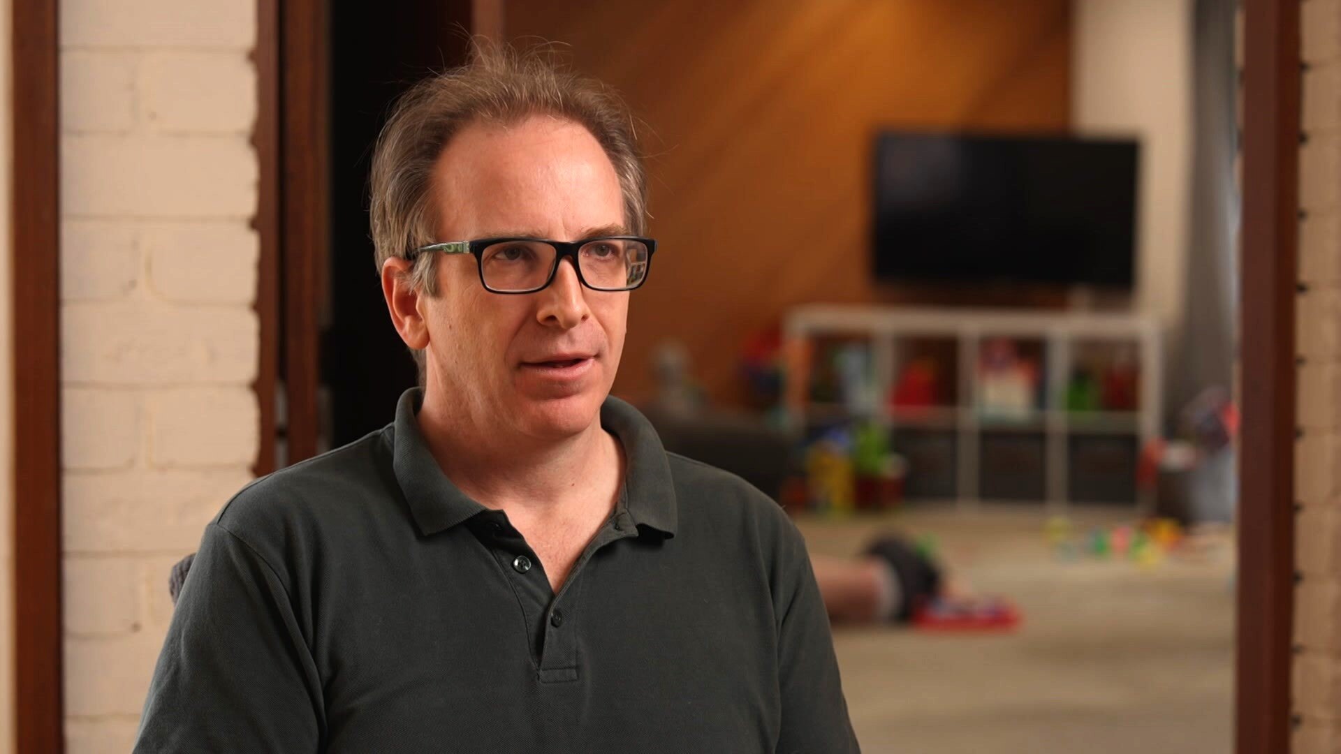 Father of two, James, sitting in a chair wearing t-shirt and glasses.