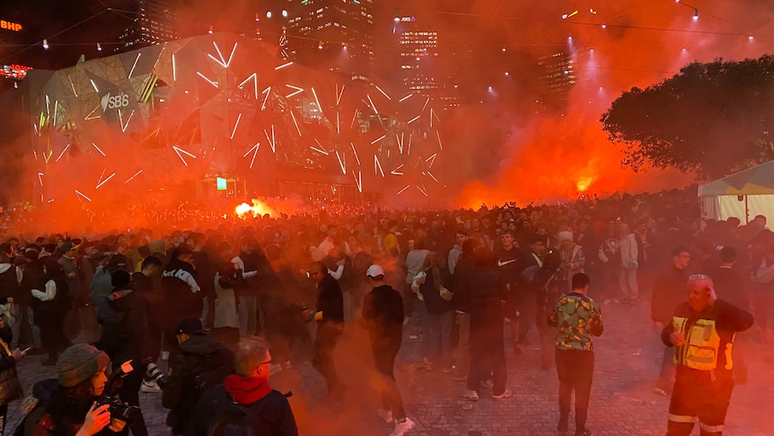 A hazy red sky over federation square full of people 