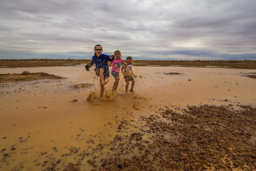 Three kids splash in puddles in Birdsville.