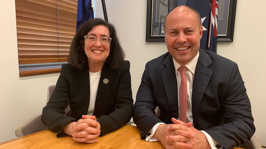 Gina Cass-Gottlieb sits next to Josh Frydenberg, both smiling with the Australian flag behind