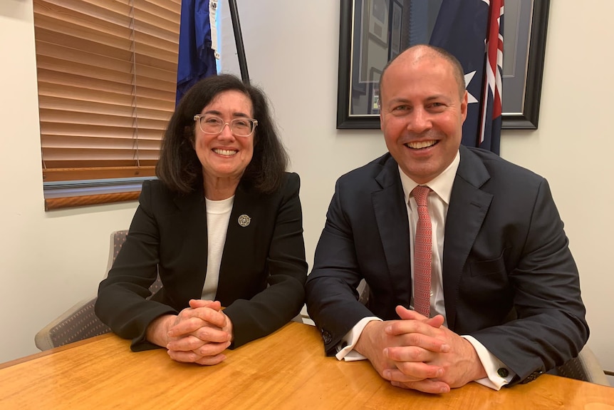 Gina Cass-Gottlieb sits next to Josh Frydenberg, both smiling with the Australian flag behind