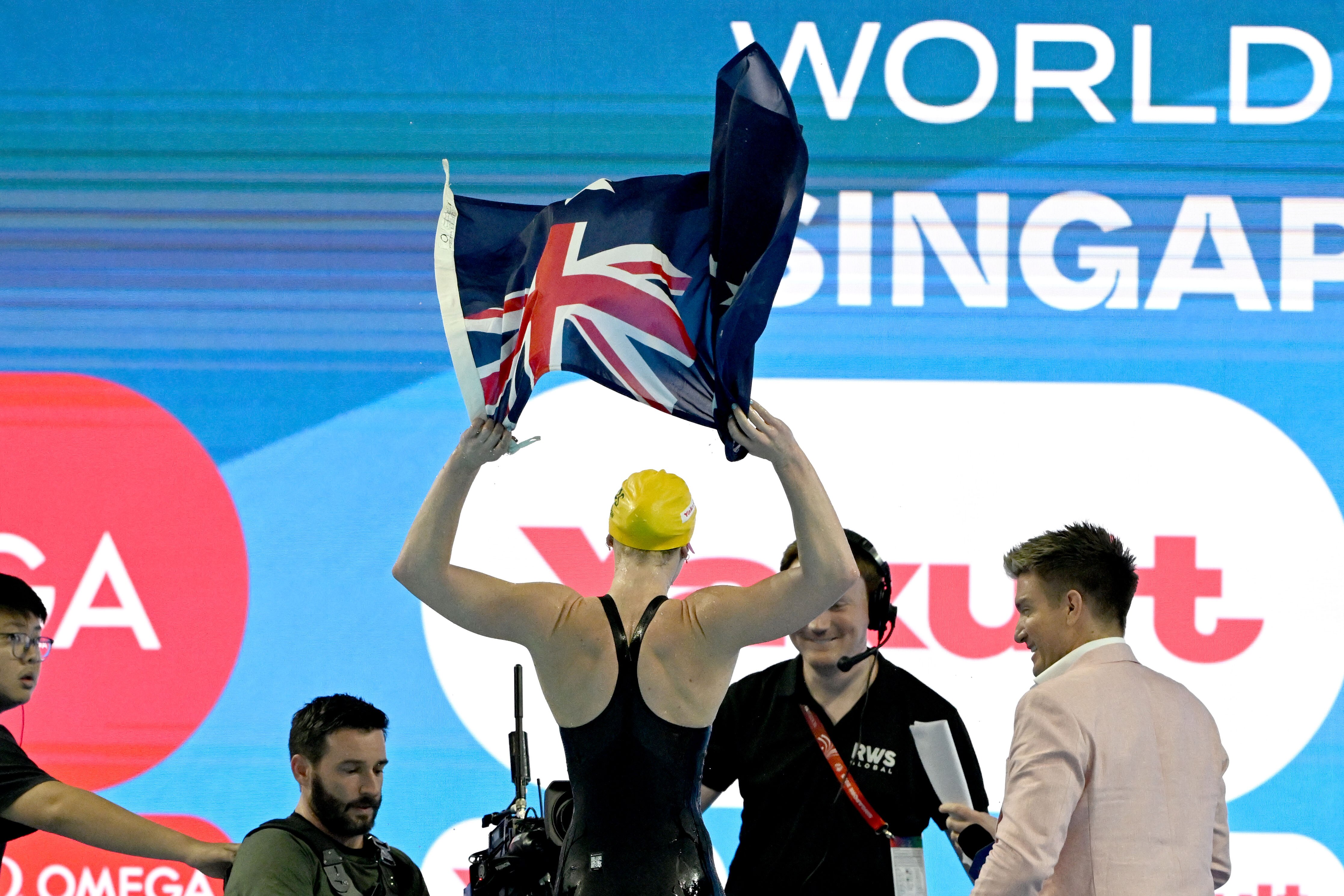Australian swimmer Mollie O'Callaghan, seen from behind, holds the Australian flag above her head after the 200m freestyle.