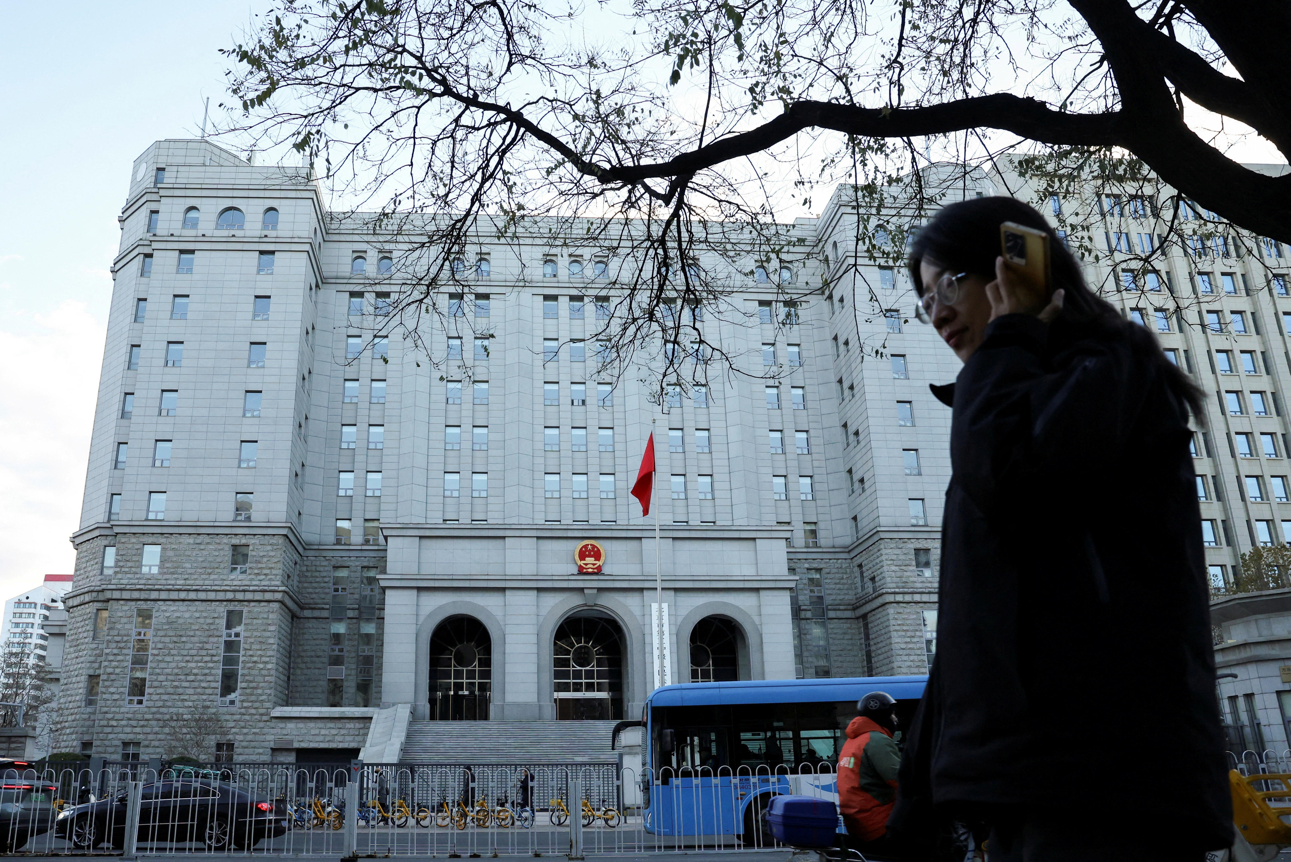 A woman holds her phone to her ear as she walks past a large multi-storey white building