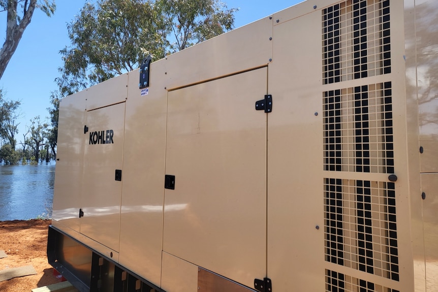 A large power generator on the bank of a swollen river.