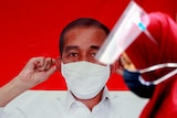 A woman wearing a protective face mask and a face shield walks past a banner depicting Indonesian President Joko Widodo.