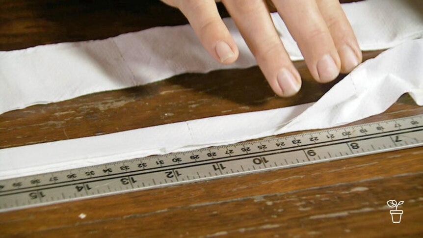 Hand measuring out folded paper along metal ruler