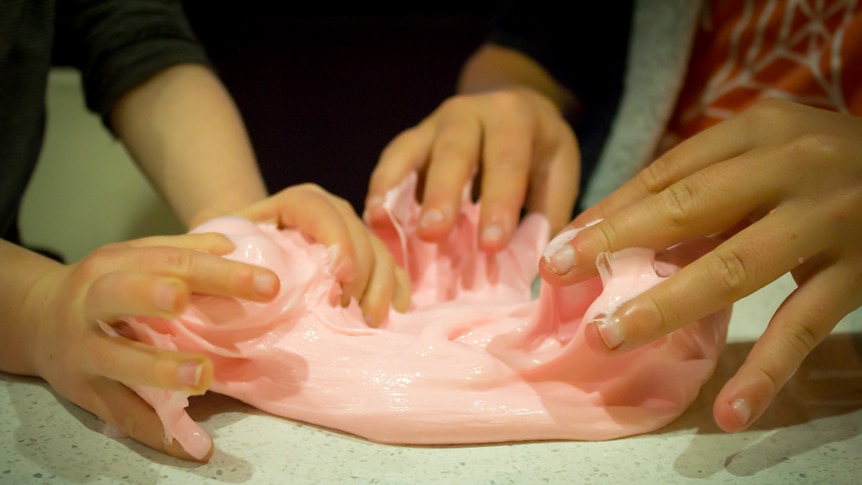 Children's hands playing with pink slime.