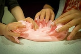 Children's hands playing with pink slime.