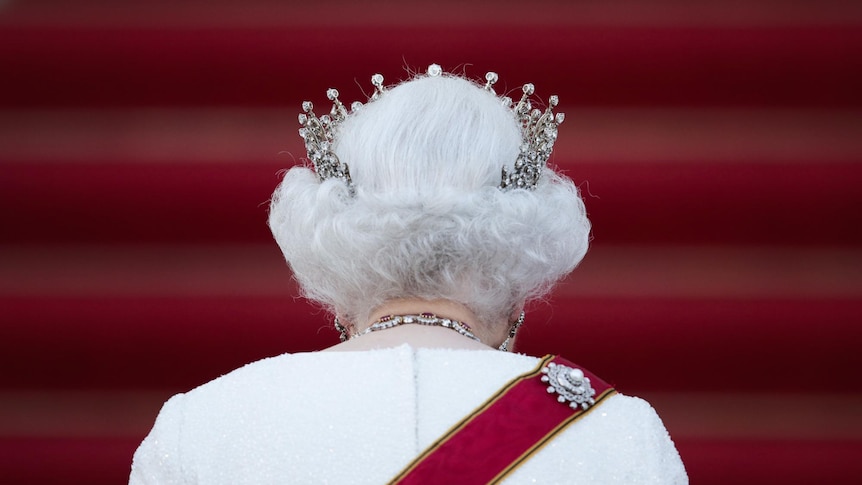 The back of Queen Elizabeth II walking up red-carpeted stairs