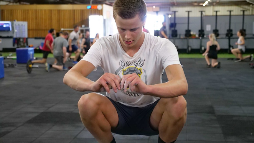 A 17 year old boy squats on box on the gym.