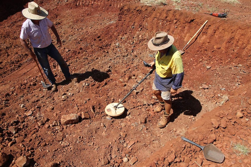 Two men stand in a ditch of red dirt.