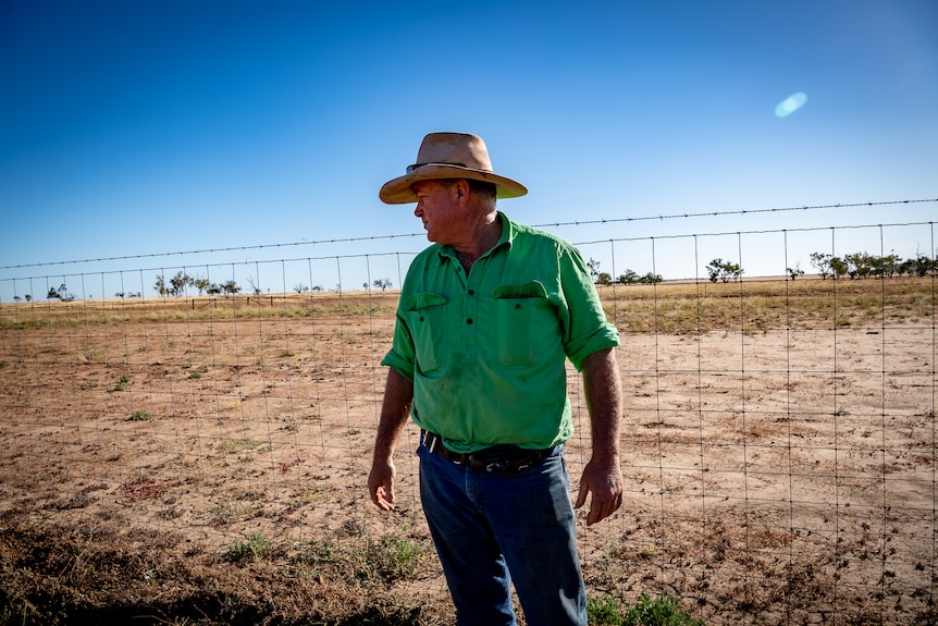 Grazier Boyd Webb is standing in front of dry country and a wire predator fence.