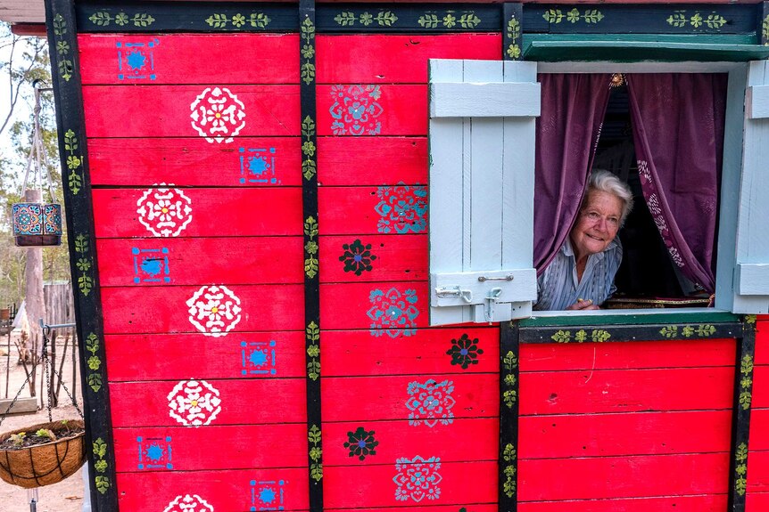A woman peers through a highly decorated traveller wagon window.