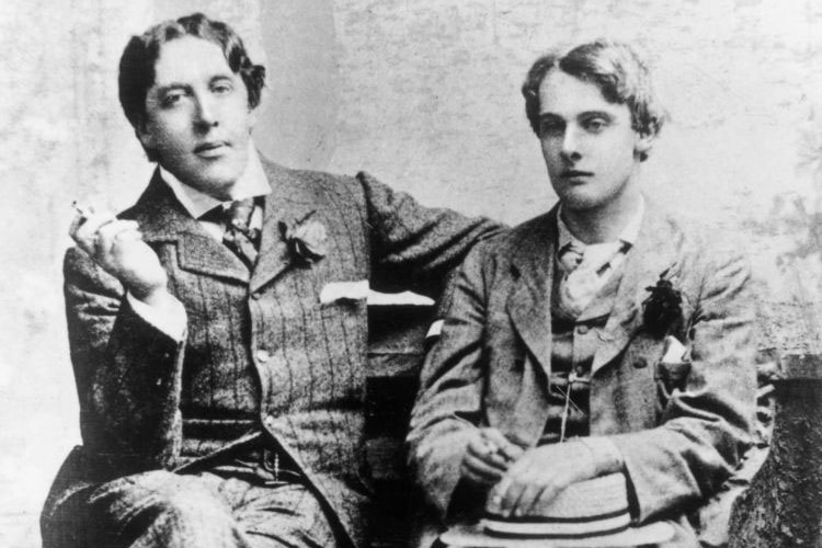Black and white photo of Irish dramatist Oscar Wilde on a couch next to Lord Alfred Douglas.