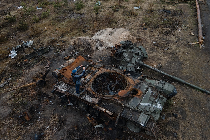 A man takes a photo of a destroyed Russian military tank