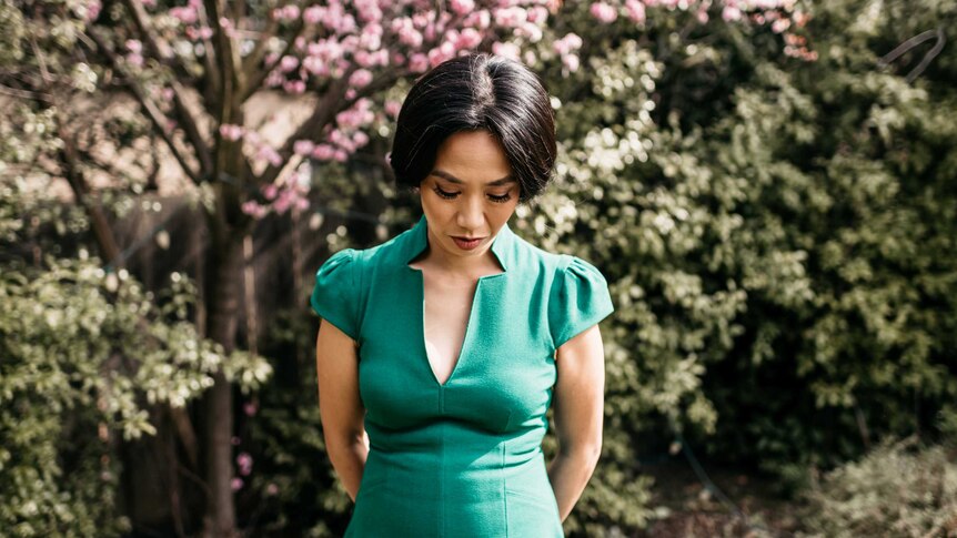 Rowena Chiu stands outside in a green dress in front of trees.