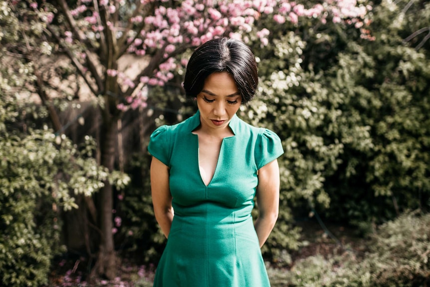 Rowena Chiu stands outside in a green dress in front of trees.