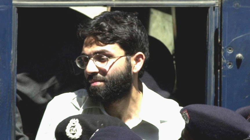 Ahmed Omar Saeed Sheikh stands near police at the front of a court.