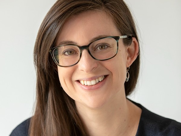 A woman with brown hair and glasses smiles at the camera