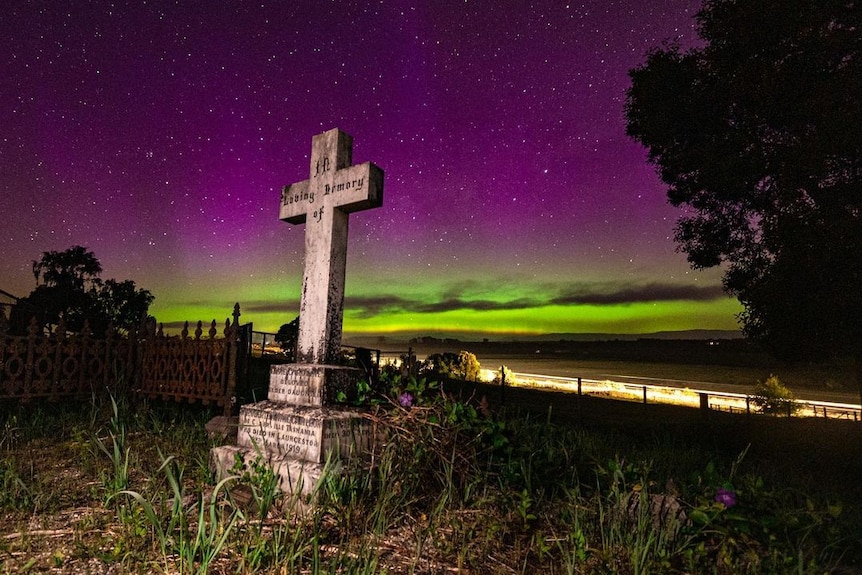 Purple and yellow lights over the night sky with a headstone in the foreground.