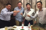 Four men are standing and lifting up their wine glasses in celebration