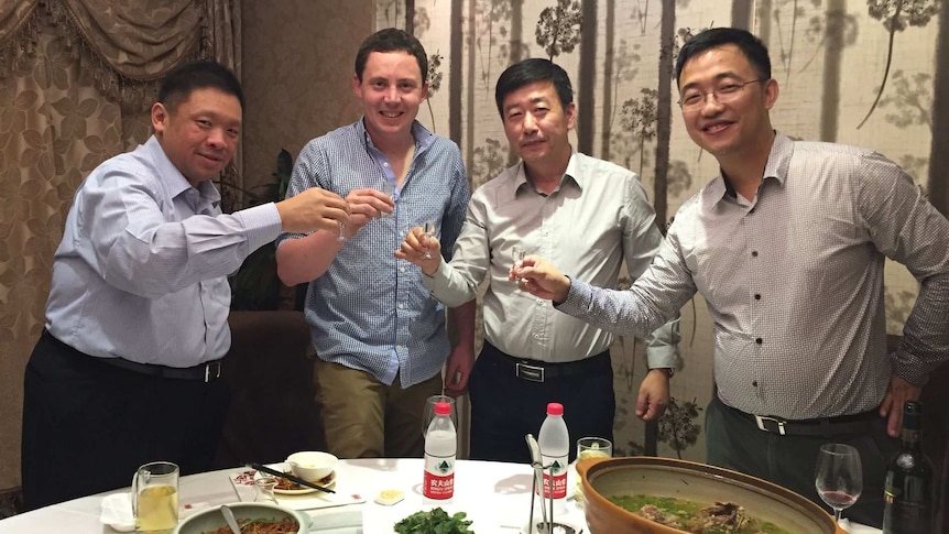 Four men are standing and lifting up their wine glasses in celebration