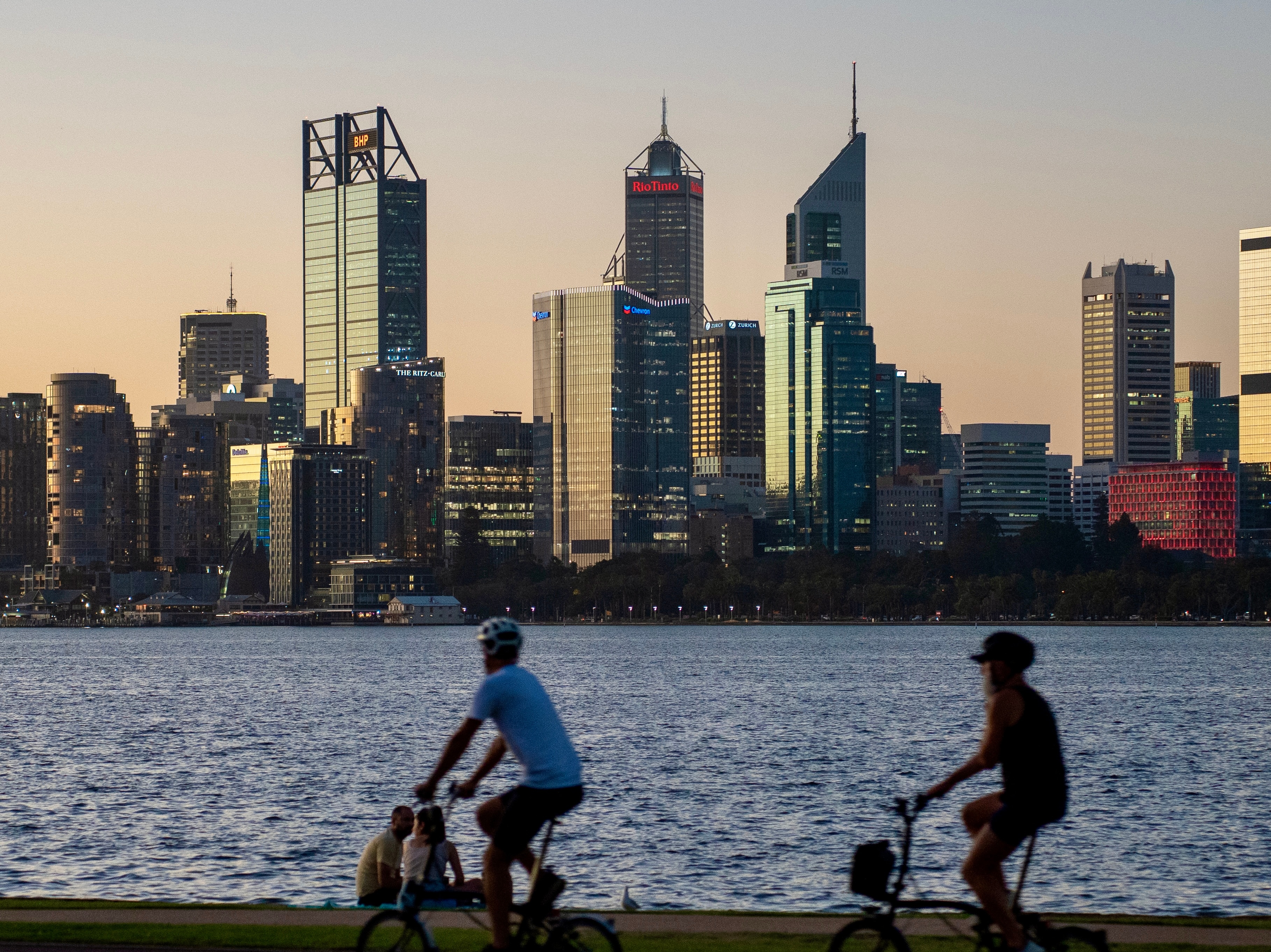 Skyscrapers in the background with the Swan River in the middle and two bicycle riders in the foreground.