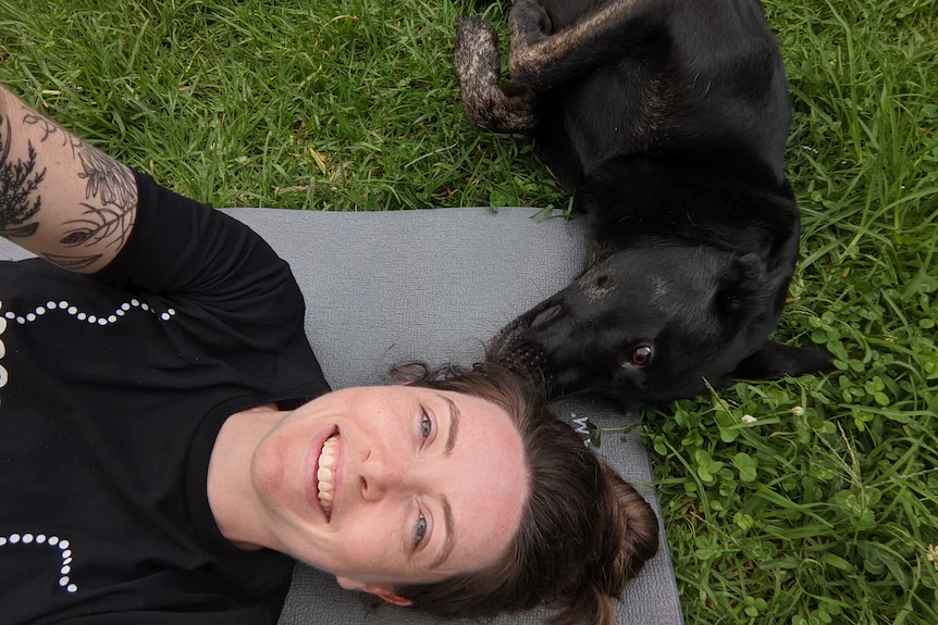 A woman lies on her back next to a dog