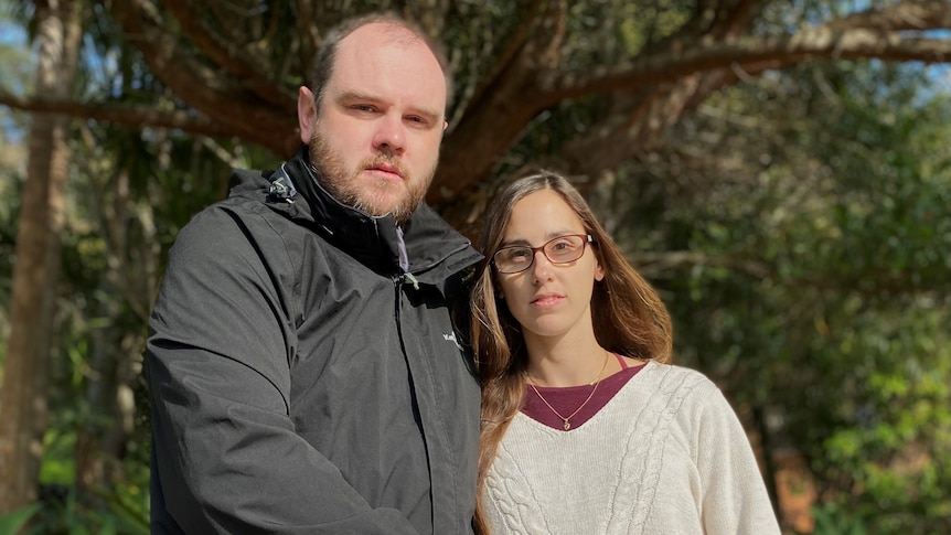 A man and a pregnant woman stand outside, looking sombre.