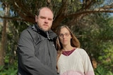A man and a pregnant woman stand outside, looking sombre.
