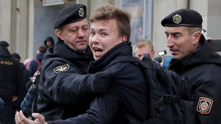 A man exclaims as he is detained by black-clad police officers