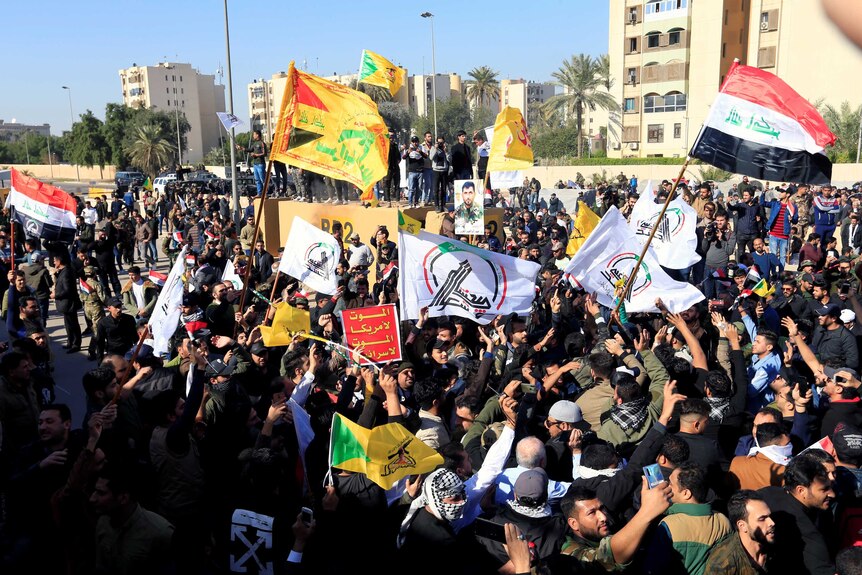 A large group of protesters and militia fighters wave Iraqi flags among other flags.