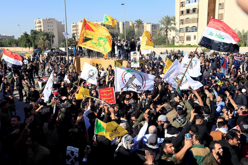 A large group of protesters and militia fighters wave Iraqi flags among other flags.