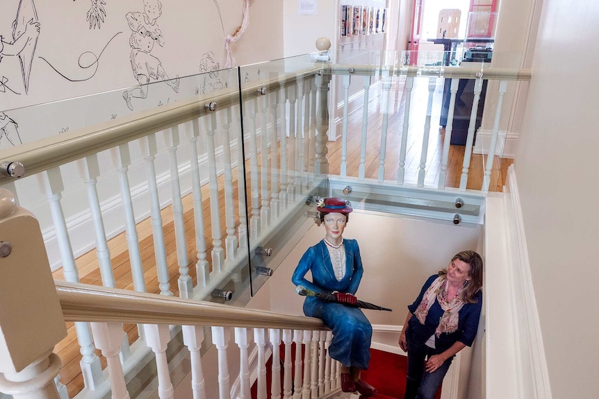 A woman stands in a stairwell with a life-size model of the character Mary Poppins.
