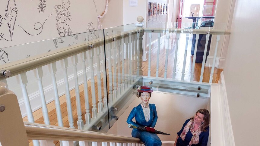 A woman stands in a stairwell with a life-size model of the character Mary Poppins.
